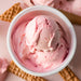 Pink ice cream in a white bowl with waffle cookies on a pink background